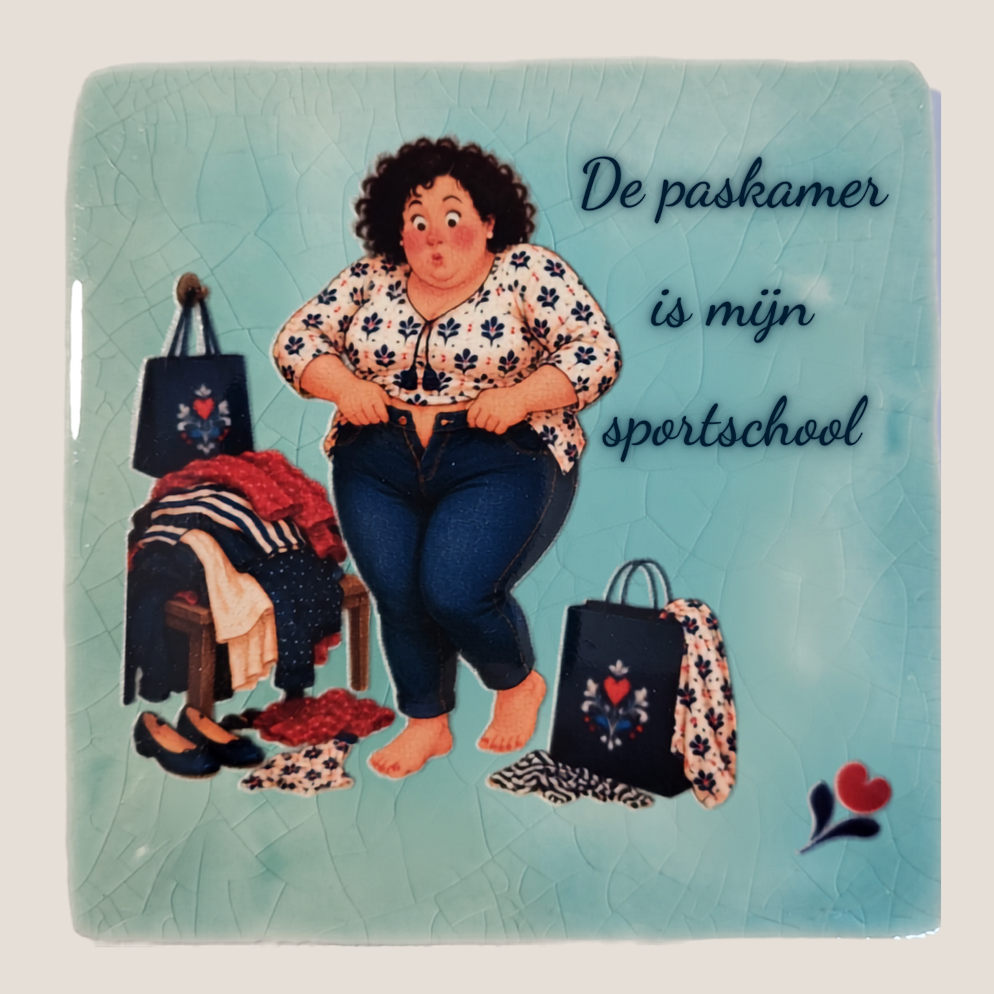 Keramisch tegeltje van De Dametjes van Fryslân met Tryntsje die een spijkerbroek probeert dicht te krijgen en de quote 'De paskamer is mijn sportschool'.